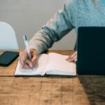 man taking notes in planner near laptop at table