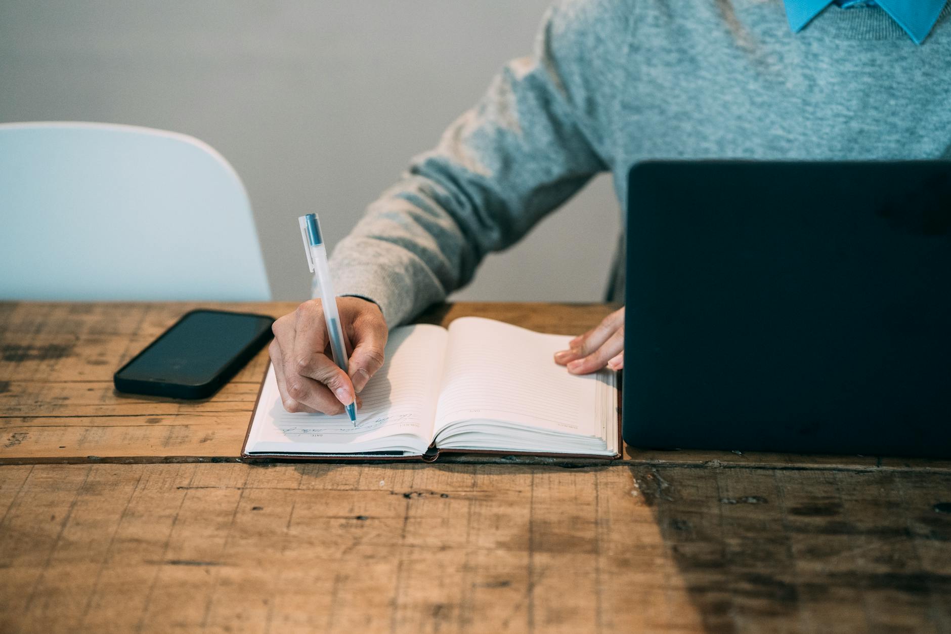 man taking notes in planner near laptop at table