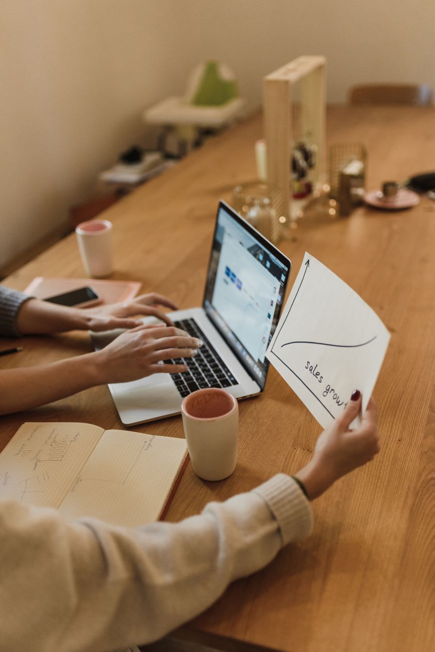 people sitting at the table using a laptop and looking at a piece of paper with a chart