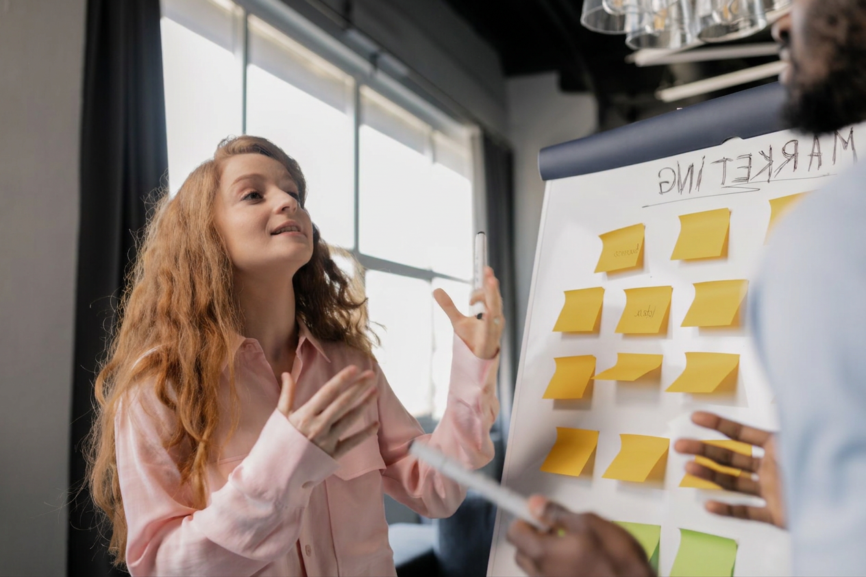 pexels-photo-7710084 a woman talking about marketing near a board with post its