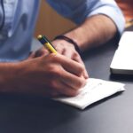 person writing on paper using yellow and black pen